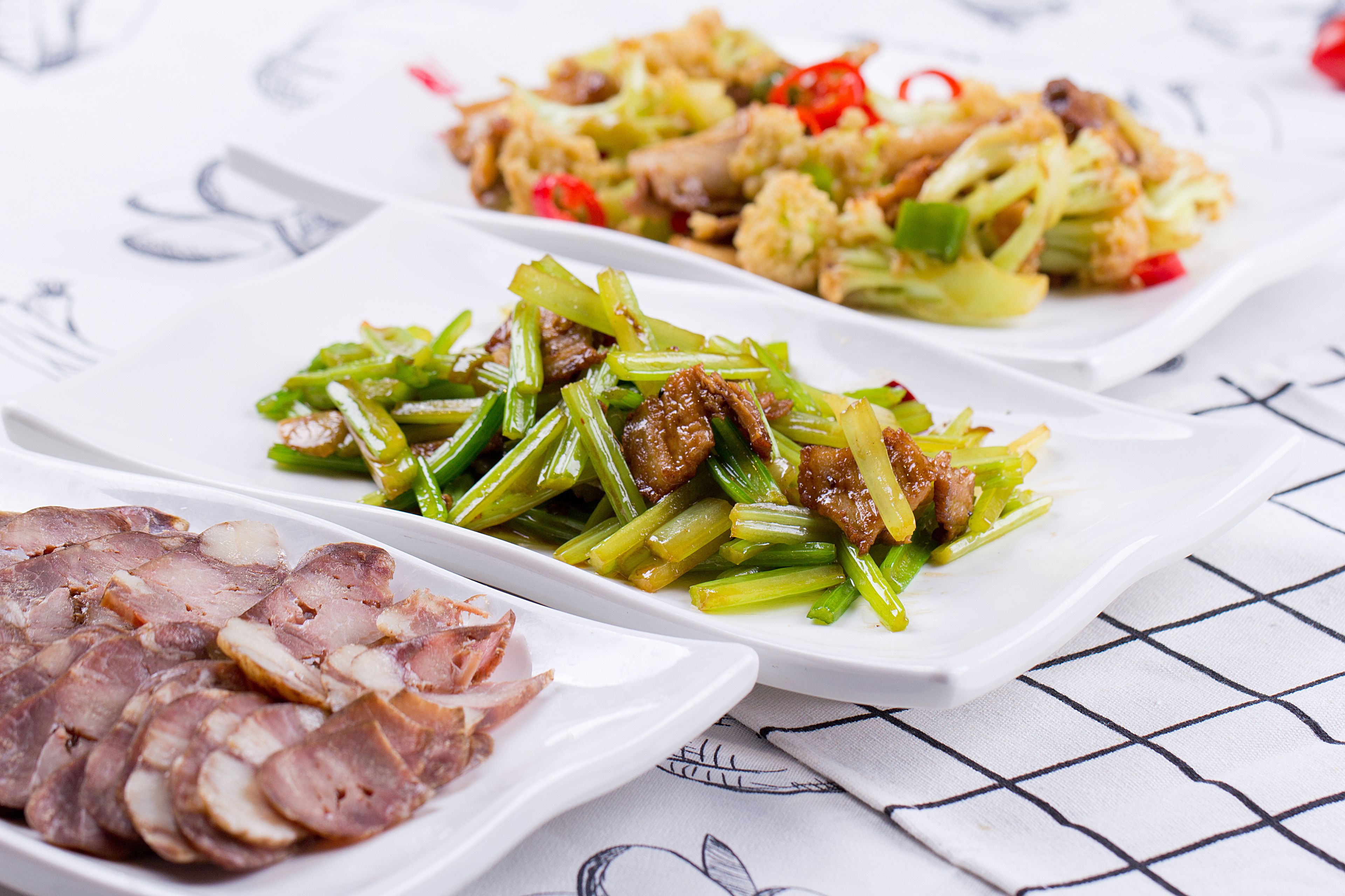 Three white rectangular plates with food, placed on a table with a grid pattern.