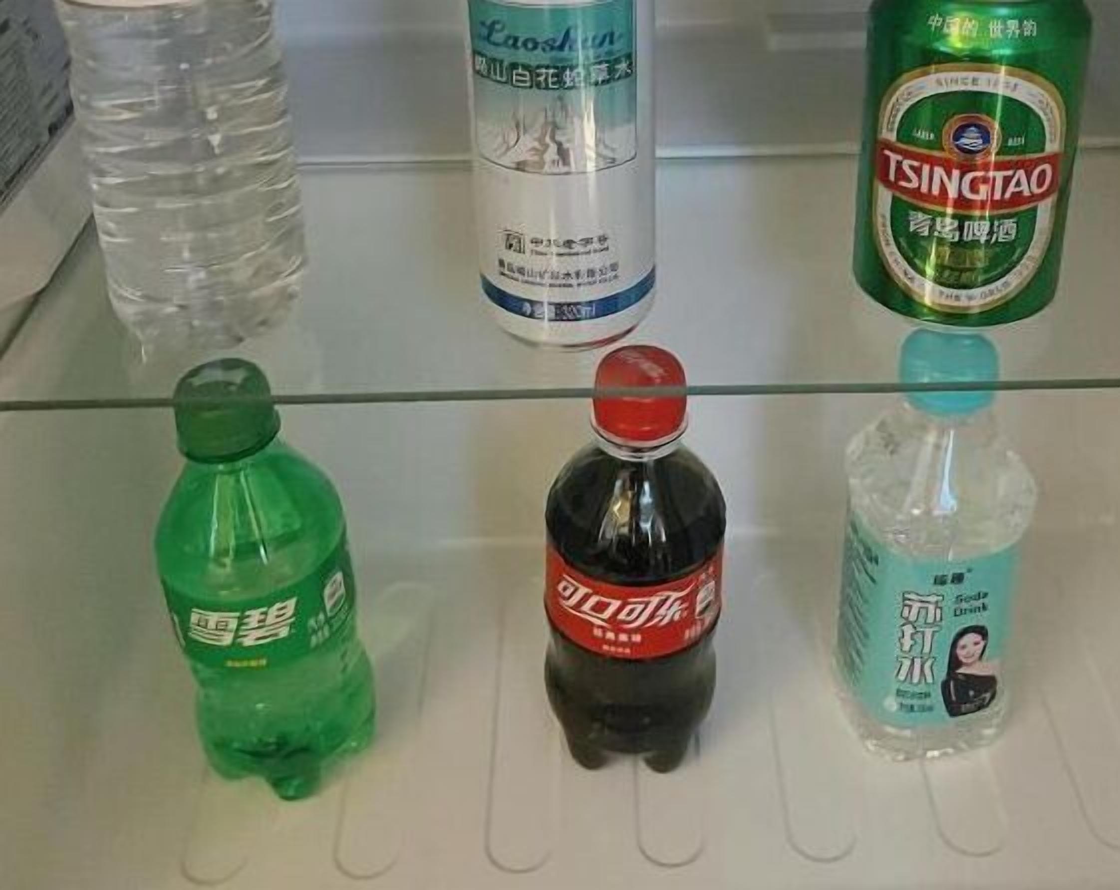 A refrigerator shelf with various beverages including a green bottle, a black bottle, and a clear bottle with a blue label.
