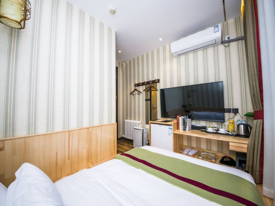 A hotel room with a bed, a desk with a television, a radiator, and a wardrobe.