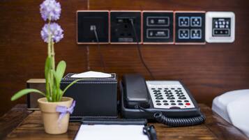 A wooden nightstand with a black telephone, a notepad, and a potted plant.