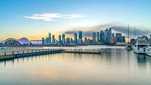 A waterfront cityscape with modern skyscrapers, a marina with boats, and a distinctive curved building. - MG Hotel - St. Michael's Cathedral, Qingdao (Qingdao)