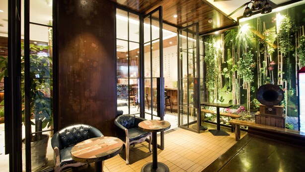 A modern interior with a wooden ceiling, glass doors, and a green wall with plants. There are two chairs and a small table. - MG Hotel - St. Michael's Cathedral, Qingdao (Qingdao)