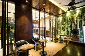 A modern interior with a wooden ceiling, glass doors, and a green wall with plants. There are two chairs and a small table. - MG Hotel - St. Michael's Cathedral, Qingdao (Qingdao)