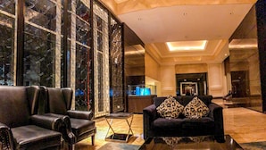 A lobby with leather sofas, a glass partition, and a reception desk. - 1 Bedroom Apartment Casa Grande Residence by Travelio (Jakarta)