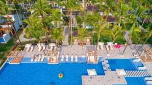 Una amplia piscina con sillones de descanso y sombrillas, rodeada de palmeras y edificios de hotel.
