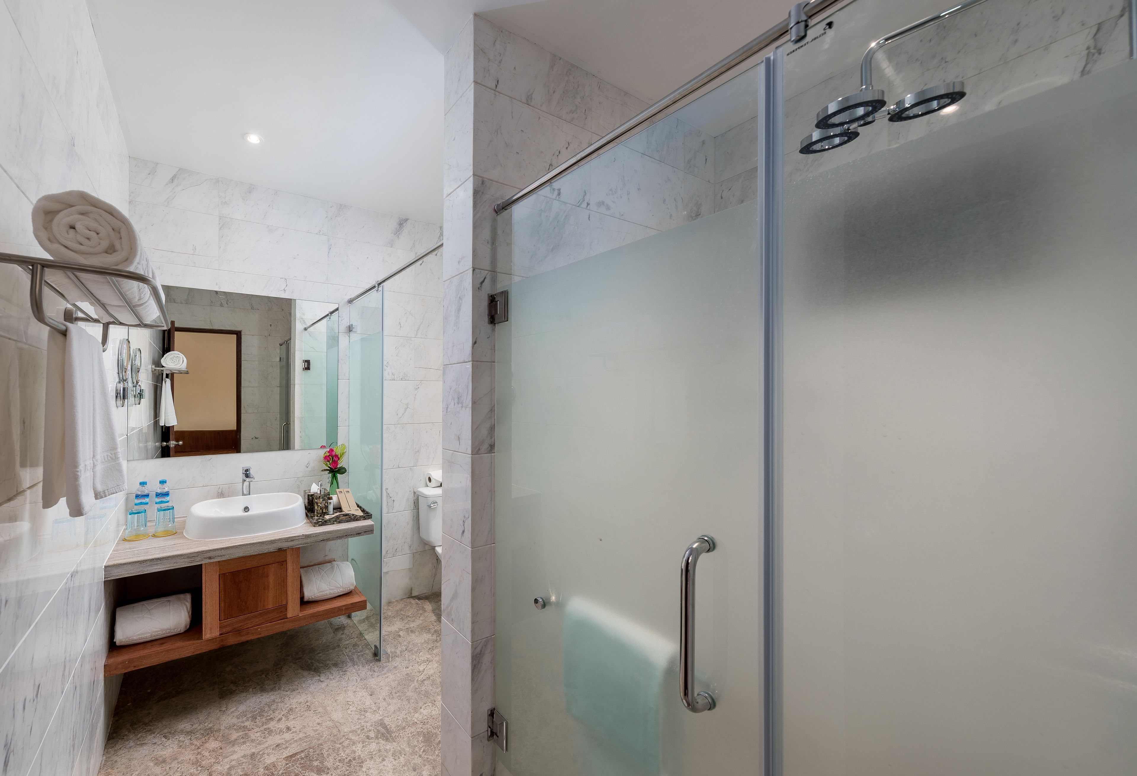 A modern bathroom with a glass shower enclosure, a marble-tiled vanity, and a wooden cabinet.