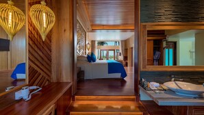 Habitación de hotel moderna con escalera de madera, una cama grande con ropa de cama azul, un área de descanso con vistas y un baño con lavamanos y espejo amplios.