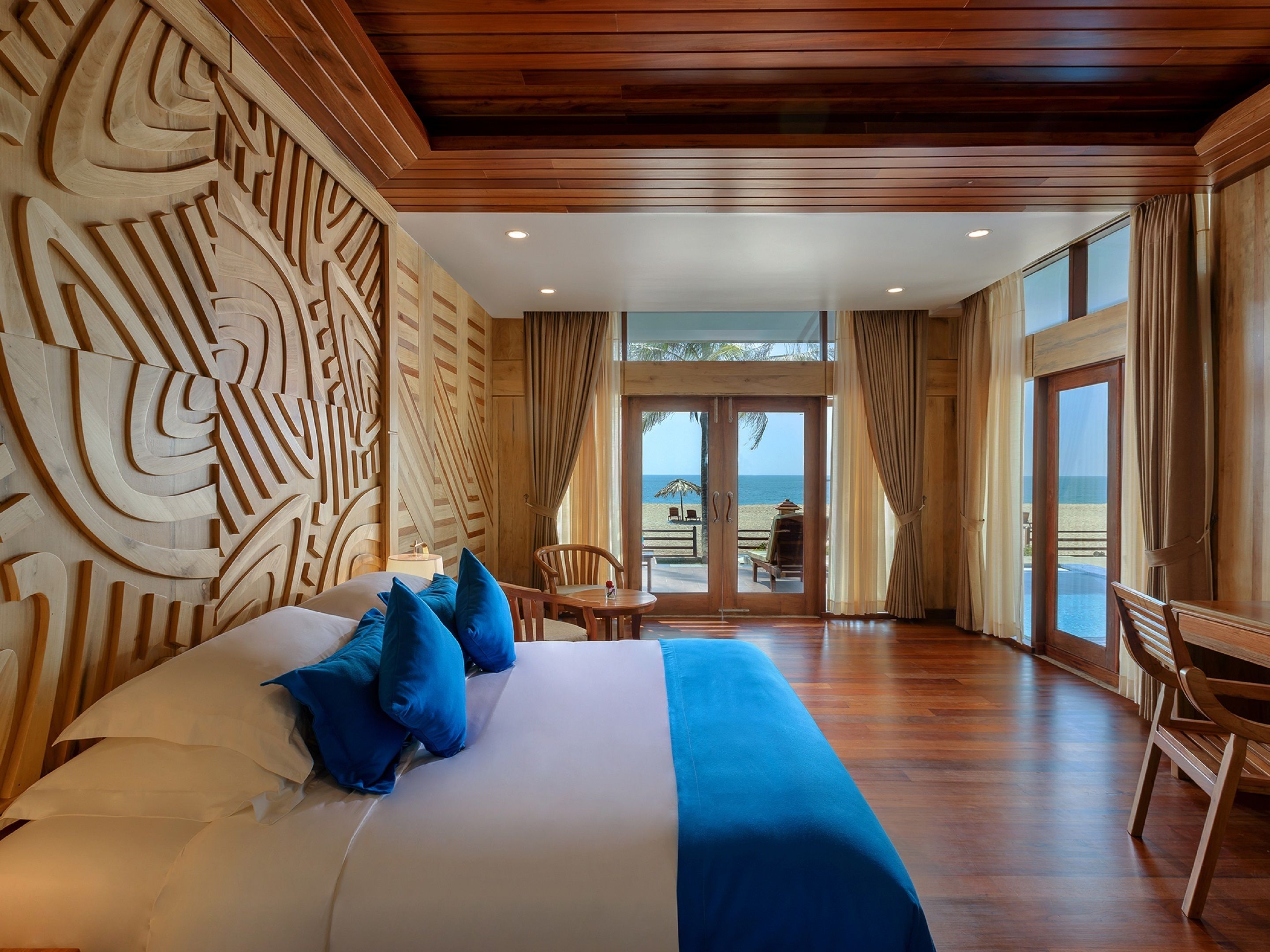 A spacious room with a large bed, wooden headboard, and a view of the beach through the glass doors.