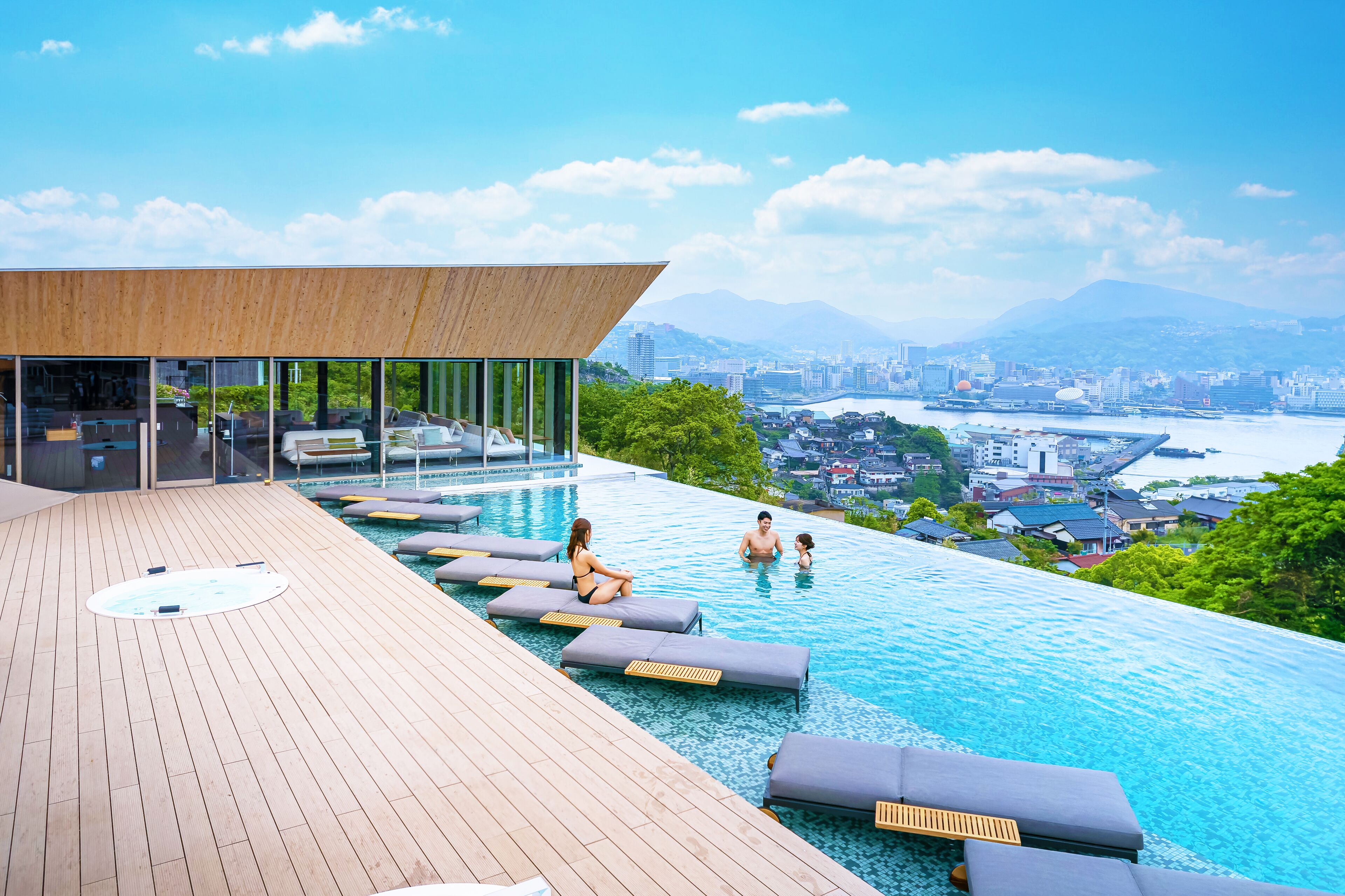 An infinity pool with lounge chairs, a wooden deck, and a city view.