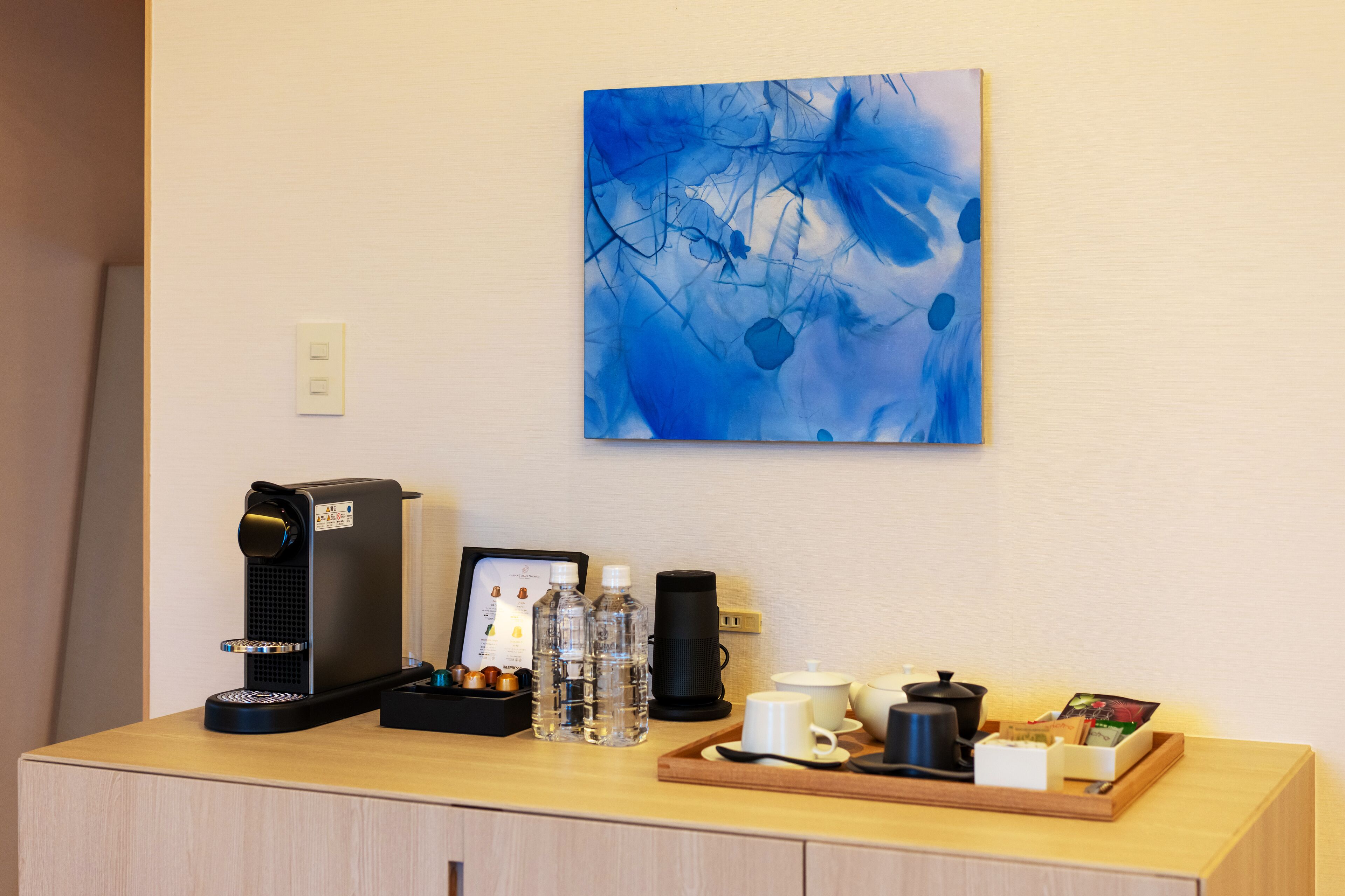 Een koffiehoek met een koffieapparaat, waterflessen, een koffiekan, bekers en een dienblad met een boek en een kaartje.