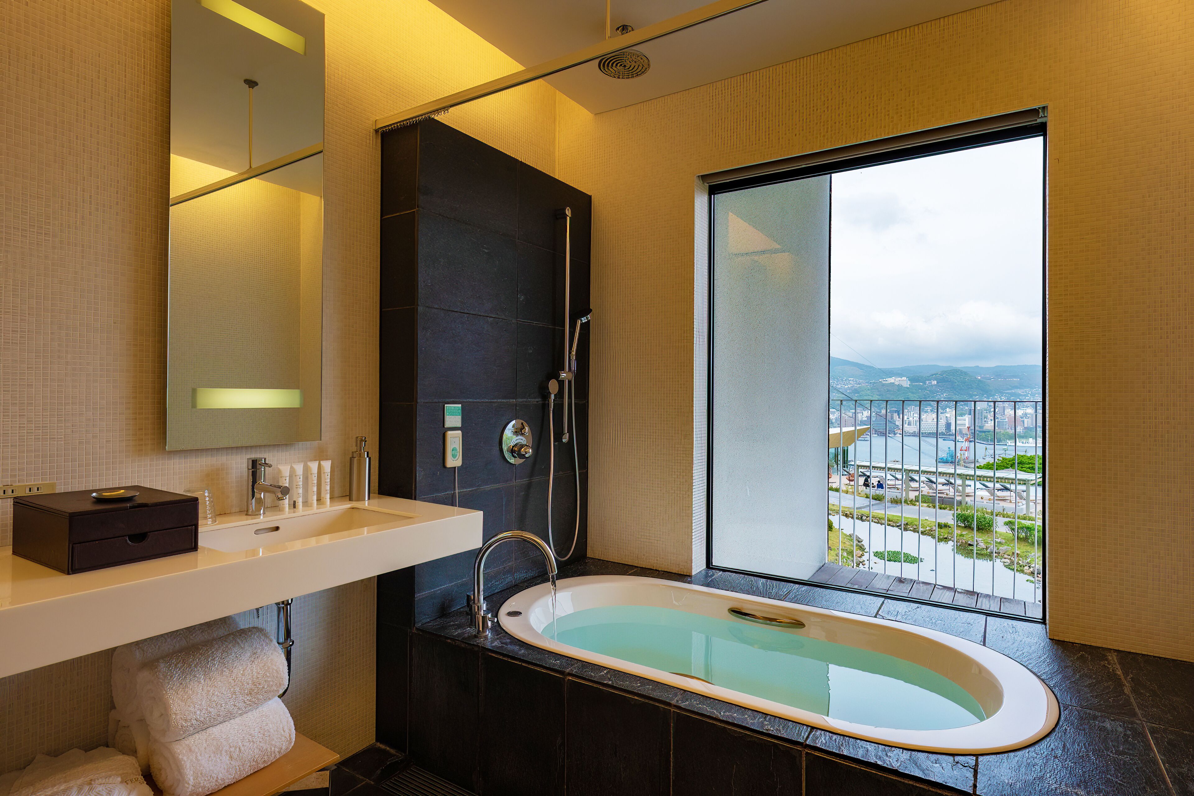 A modern bathroom with a bathtub, a large mirror, a sink, and a view of a cityscape through a large window.