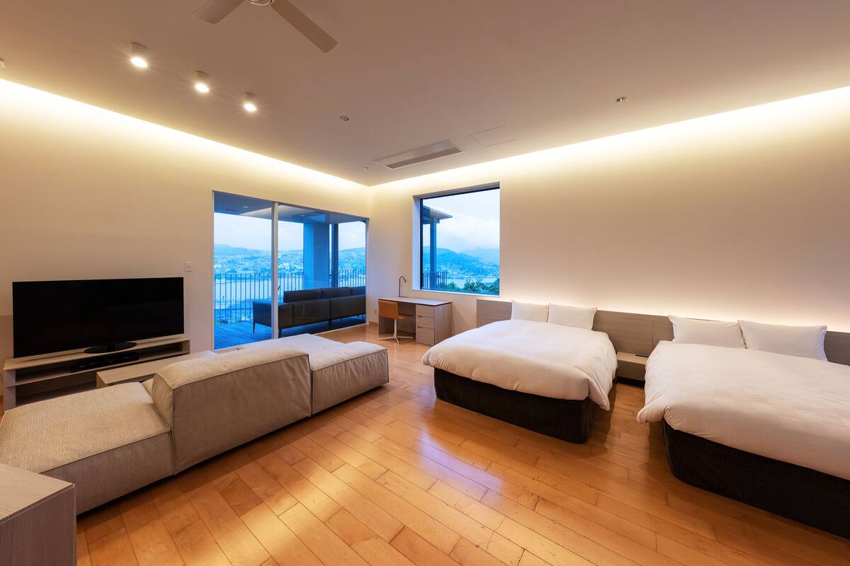 A modern hotel room with a large flat-screen TV, a sofa, a bed, and a desk.