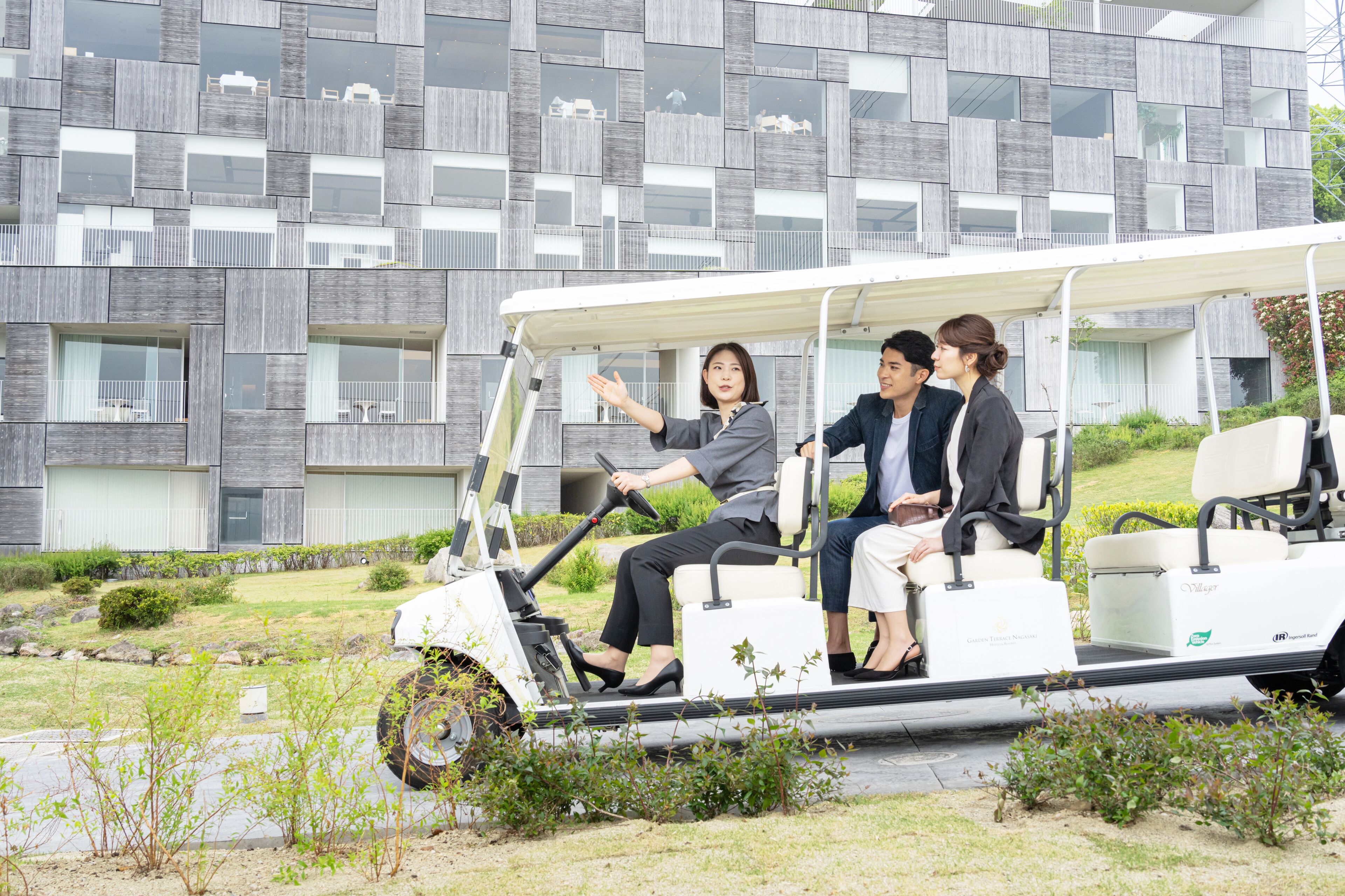 Un edificio moderno con fachada geométrica y un carrito de golf con tres pasajeros.