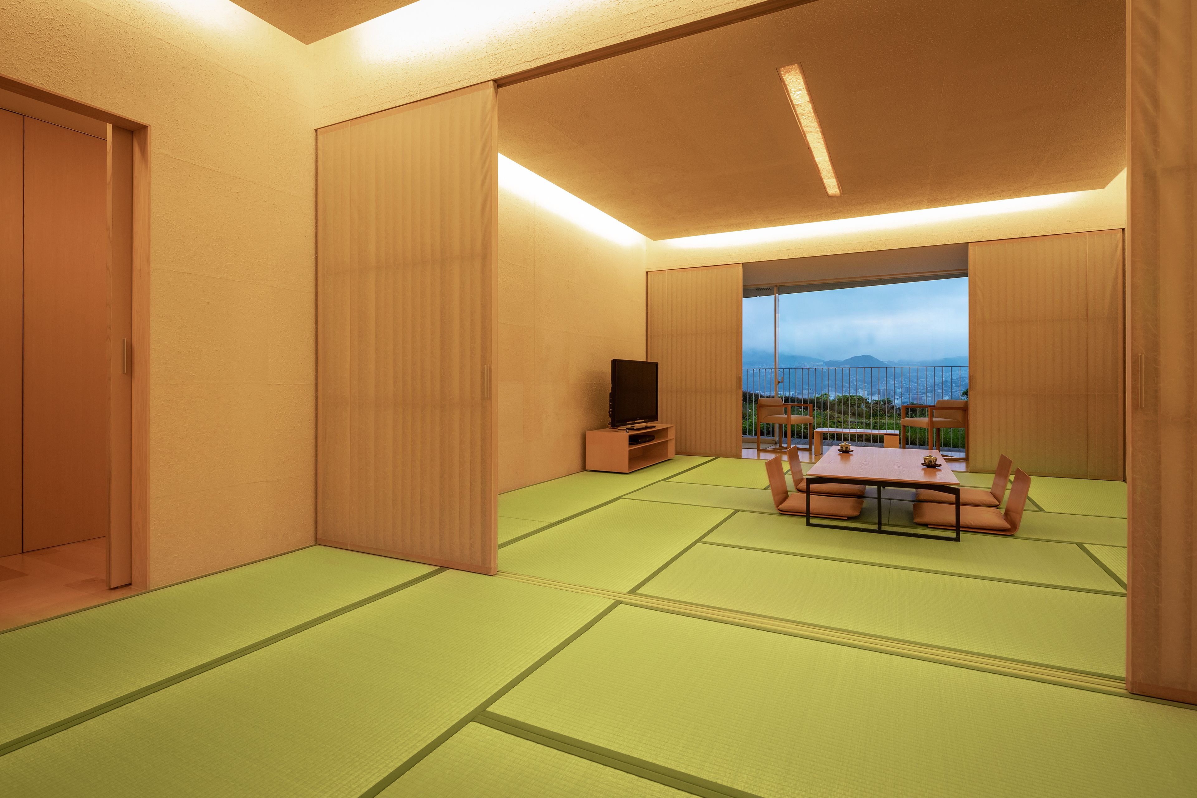 A room with tatami mats, a TV stand, a table with chairs, and a view of the city.