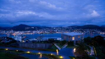 A cityscape at dusk with a prominent modern building, a waterfront, and surrounding hills.