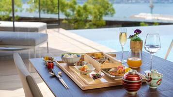 A dining table with various dishes and drinks, set against a scenic view of a body of water and greenery.