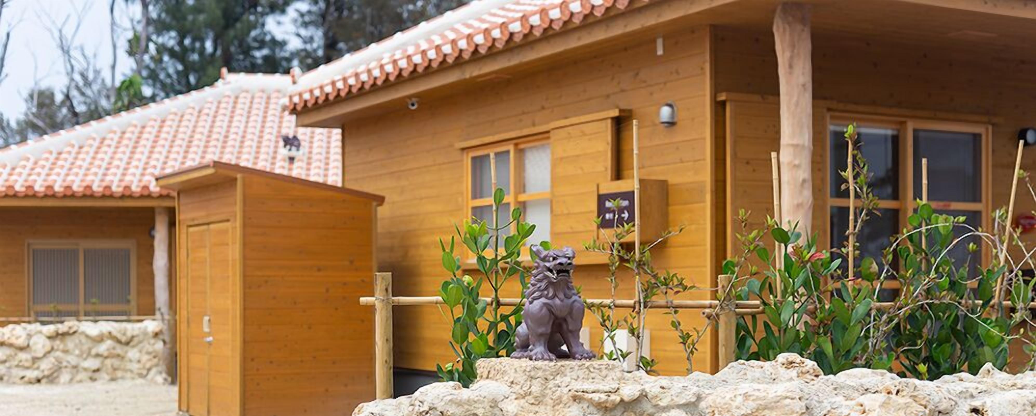 A wooden cabin with a tiled roof, a small statue of a lion, and a stone wall in front.