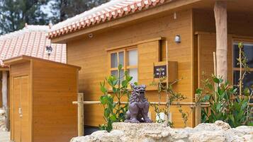 A wooden cabin with a tiled roof, a small statue of a lion, and a stone wall in front.