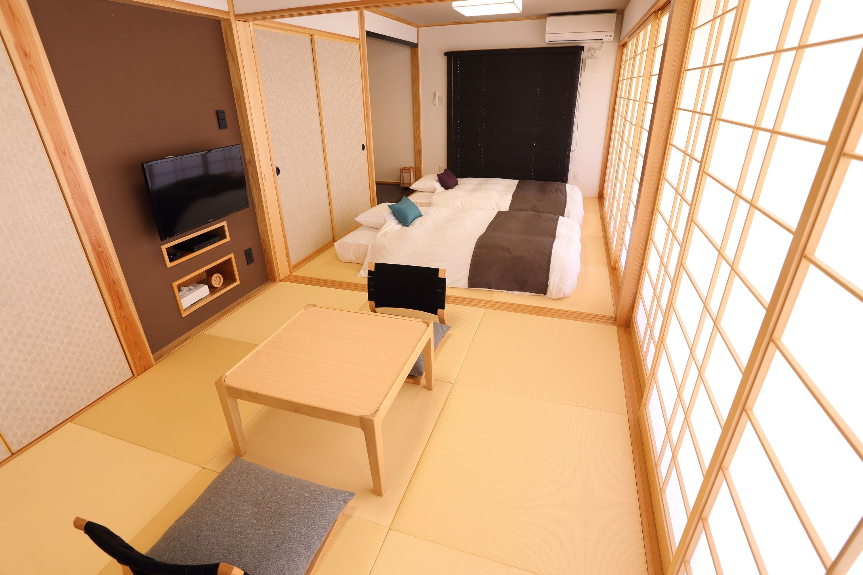 A traditional Japanese-style room with tatami flooring, a bed with a dark headboard, a television, and a small wooden table.
