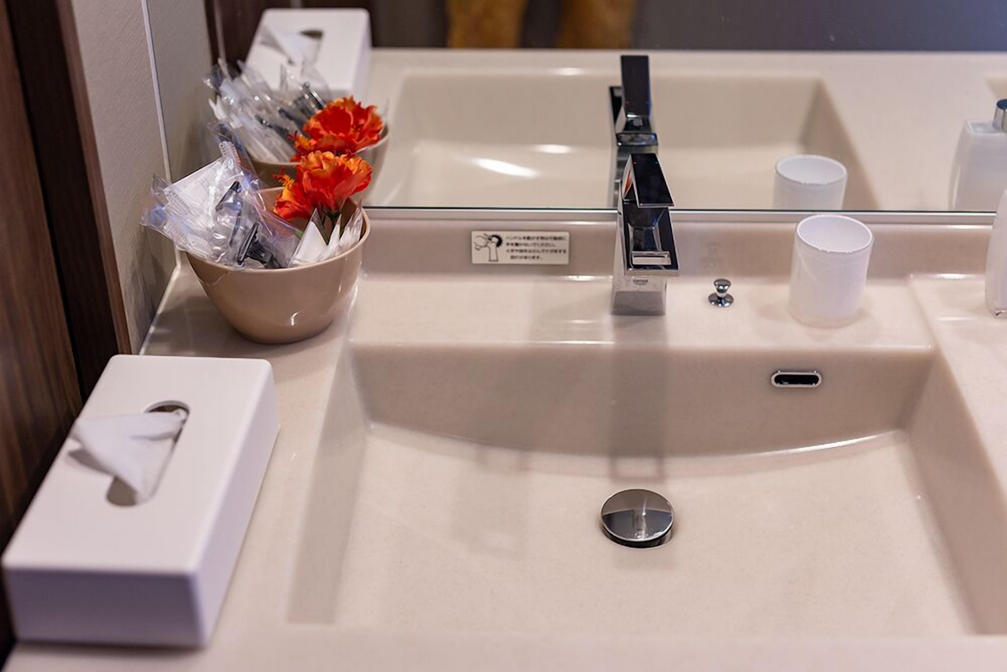 A bathroom sink with a mirror, a tissue box, a cup, and a bowl with toiletries.