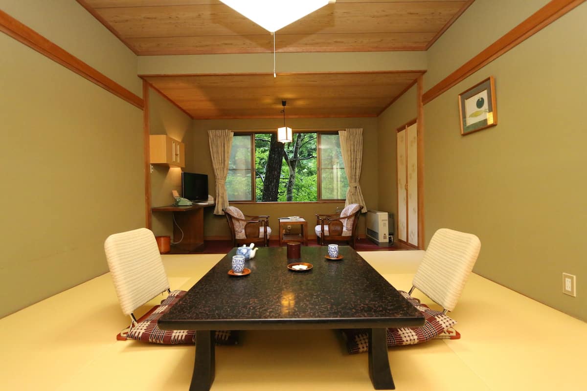 A dining room with a rectangular table, four chairs, a chandelier, and a window with curtains.