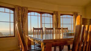 A dining area with a wooden table and chairs, large windows with curtains, and a view of the outdoors. - The Round House ~Truly Unique ~ Sleeps 14 ~ Close to CBD and Mount Panorama!
 (Bathurst)