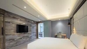 Une chambre moderne avec un grand lit, un téléviseur à écran plat fixé sur un mur en marbre et un petit bureau avec une chaise.
