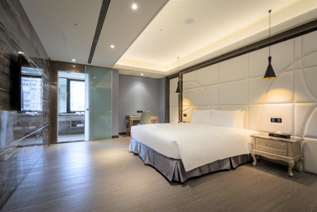 A modern hotel room with a large bed, bedside tables, a desk, and a view through a glass door.