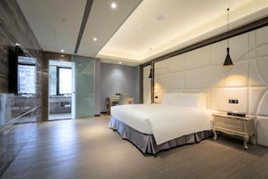 Habitación de hotel moderna con una cama grande, mesitas de noche, un escritorio y vistas a través de un ventanal.