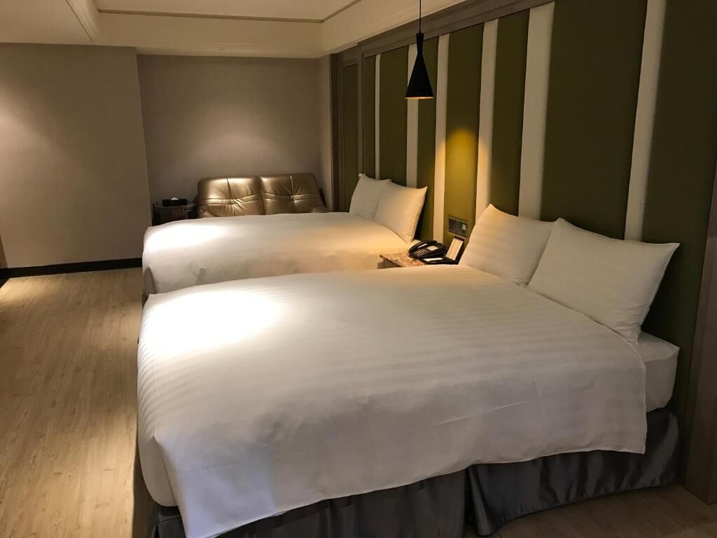 A hotel room with two beds, a wooden floor, a striped wall, and a hanging light fixture.