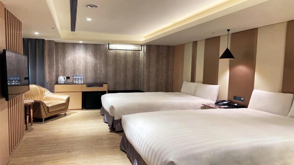 Habitación de hotel con dos camas, un escritorio, una silla y un televisor.