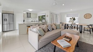 Eine moderne Küche mit integriertem Kühlschrank und Herd, ein Essbereich mit Holztisch und Stühlen sowie ein Wohnzimmer mit Sofa und Couchtisch.