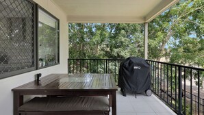Ein Balkon mit Holztisch, Bank, Grill und Blick auf Bäume.