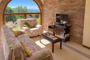 A living room with a sofa, armchair, and coffee table, a television, and a brick wall.