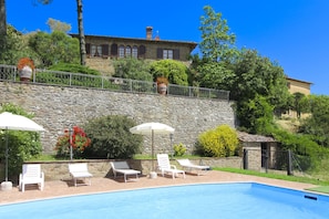 A swimming pool with lounge chairs and umbrellas, a stone wall, and a building with arched windows in the background. - Beautiful villa with a splendid panoramic view over vineyards and olive groves. Ideal for visiting T (Monte San Savino)