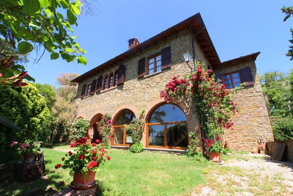 Une maison en pierre dotée de fenêtres en arc de cercle et d’un jardin agrémenté de plantes en pot.