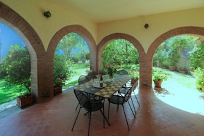 Un patio techado con una mesa a cuadros, sillas negras y plantas en macetas.