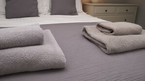 A neatly made bed with grey bedding and pillows, a folded grey towel on the bed, and a bedside table with a lamp and a drawer. - Bakers Rest, ideal for 2 families or group, centrally located in Grasmere, close to lake (Grasmere)