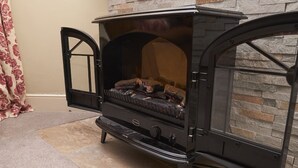 A black wood-burning stove with a stone wall backdrop, a tiled floor, and a partially open door. - Bakers Rest, ideal for 2 families or group, centrally located in Grasmere, close to lake (Grasmere)