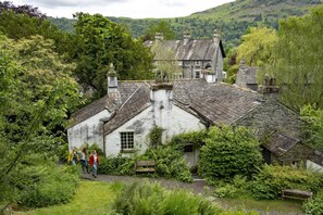 Una casa in pietra tradizionale con tetto di paglia, immersa nel verde e con dolci colline sullo sfondo.