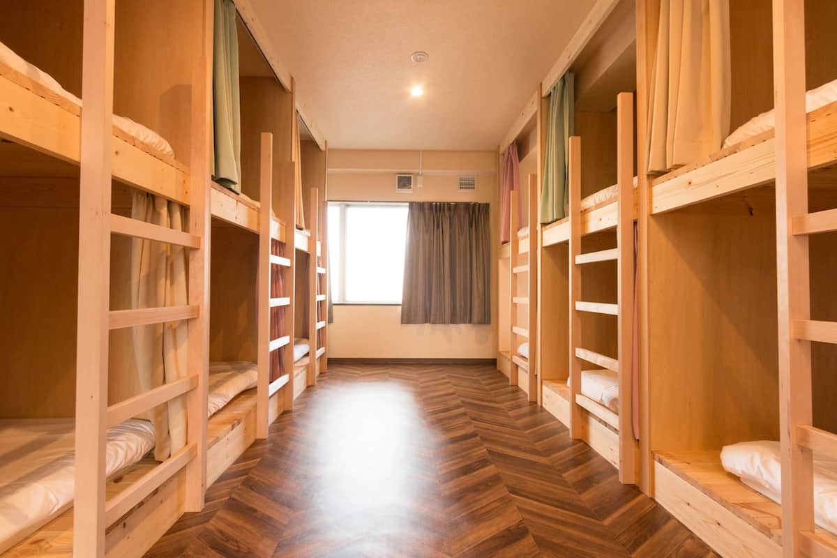 A room with bunk beds arranged in a hallway, wooden flooring, and a window with curtains.