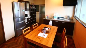 A compact kitchen with a refrigerator, microwave, and sink. There is a wooden dining table with chairs and a small cabinet with a mirror. - RED HELMET House＆Sports Bar Hiroshima - Hostel (Hiroshima)