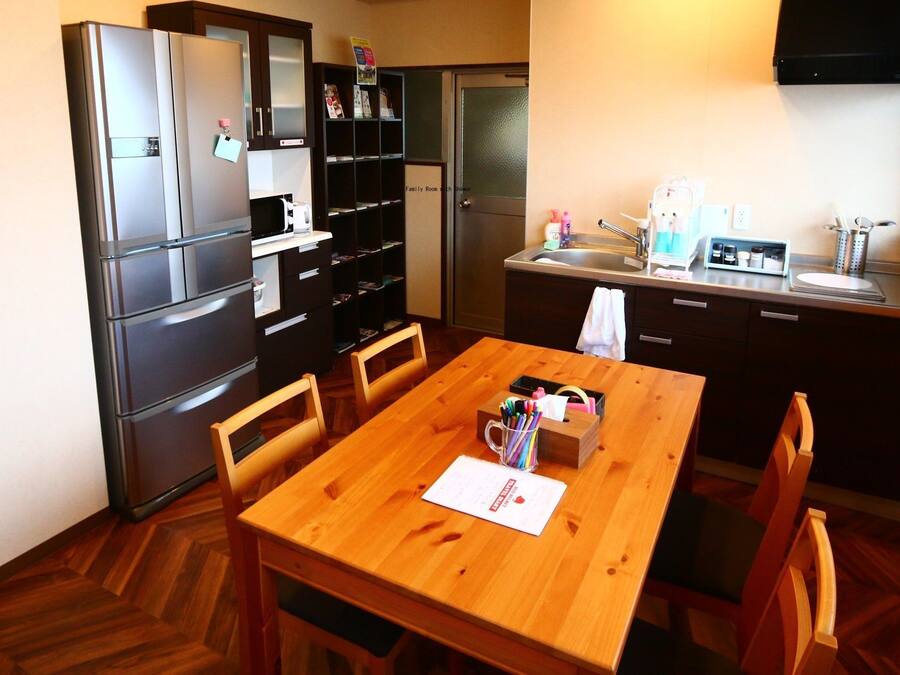 A compact kitchen with a refrigerator, microwave, and sink. There is a wooden dining table with chairs and a small cabinet with a mirror.