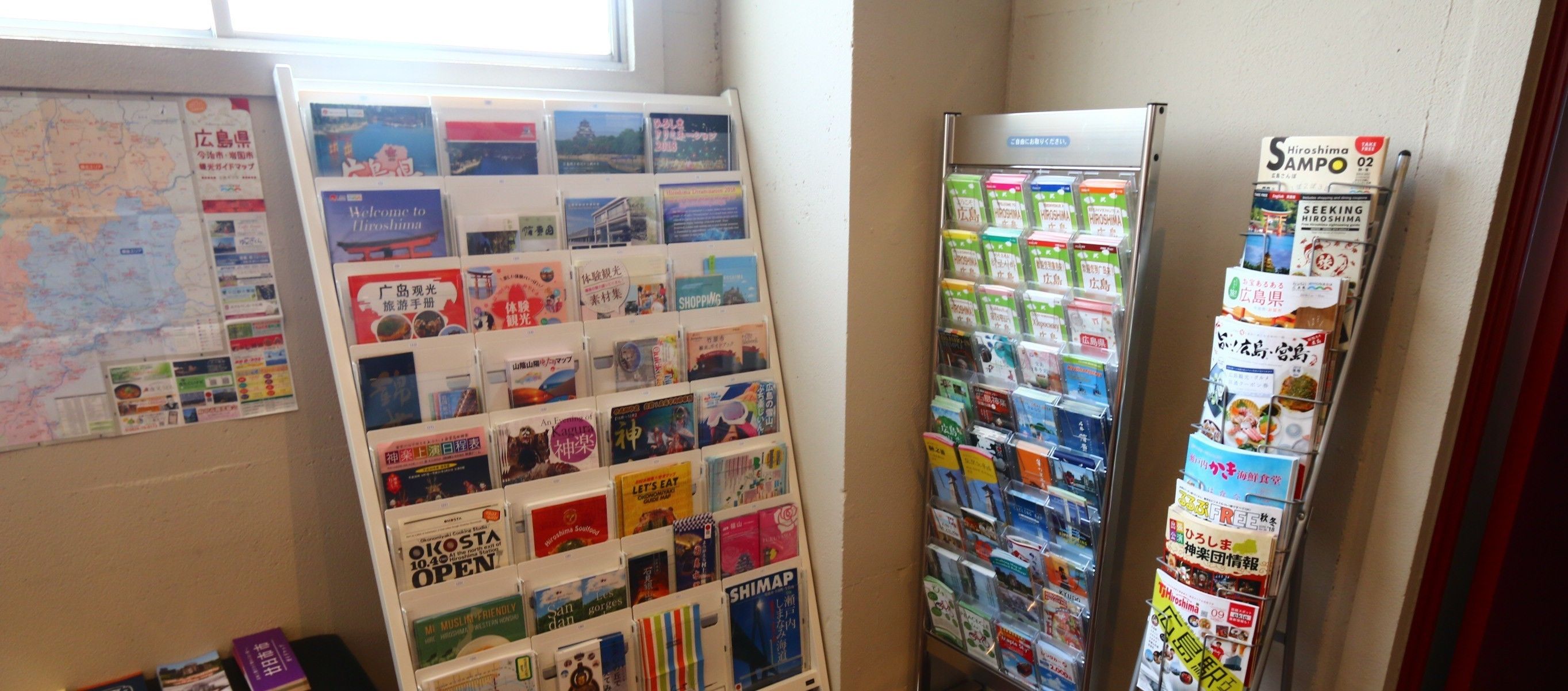 Un panneau d’affichage où sont accrochées diverses brochures de voyage et des documents d’information, un réfrigérateur orné de magazines et une carte géographique au mur.