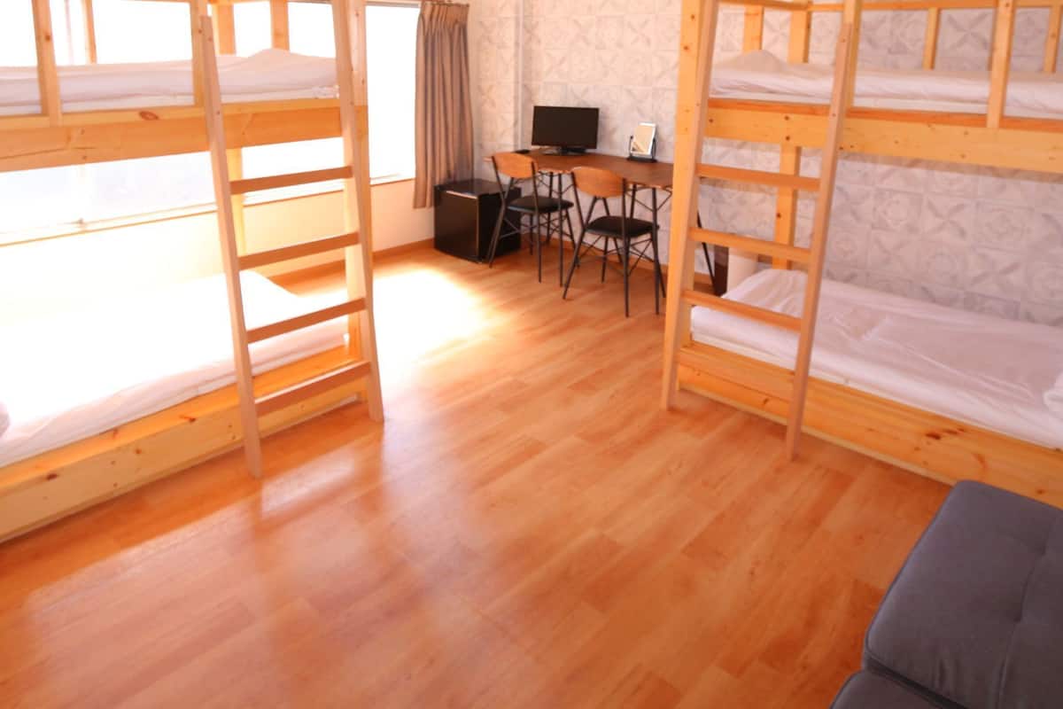 A dormitory room with bunk beds, a desk, and a chair.
