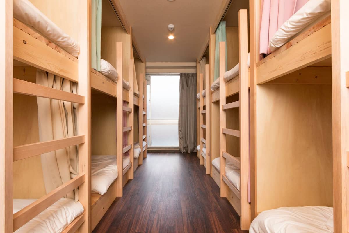 A corridor with bunk beds on both sides, wooden flooring, and a window at the end.