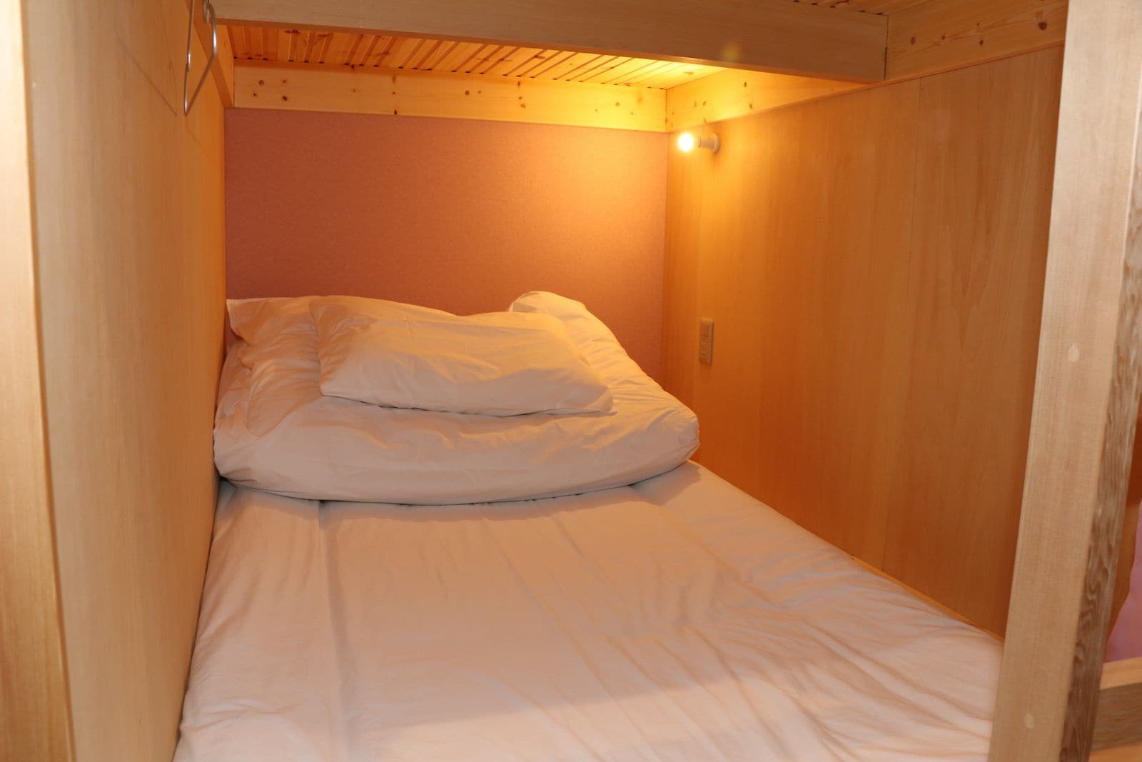 Un lit simple dans une pièce en bois avec un plafond en pente et un luminaire fixé au mur.
