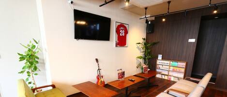 Una sala de estar moderna con un televisor de pantalla plana, una guitarra roja, un sofá, una mesa de madera y una planta.