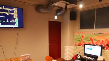 A room with a television displaying a video game, a computer monitor, and a baseball-themed wall mural.