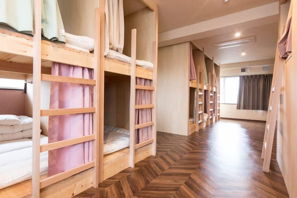 A room with bunk beds, wooden flooring, and a window with curtains.